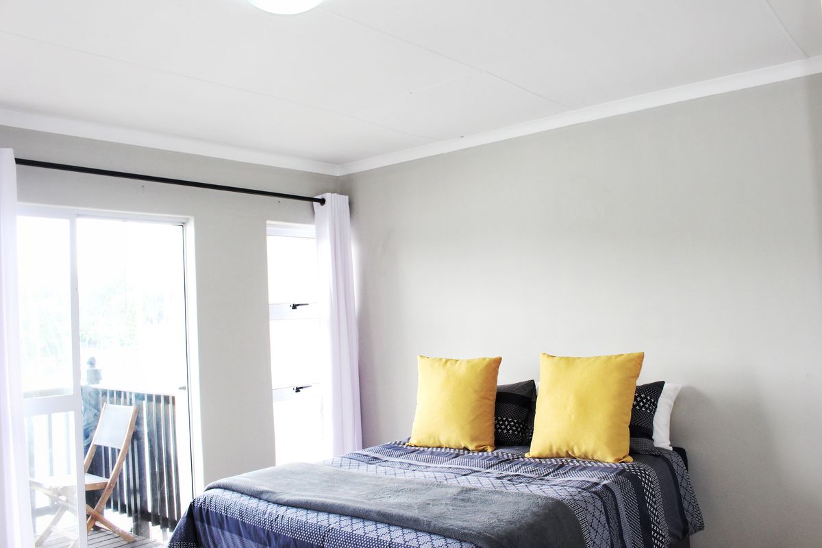 A bright bedroom featuring neutral walls, a ceiling light fixture, and a sliding glass door providing access to an outdoor balcony area.