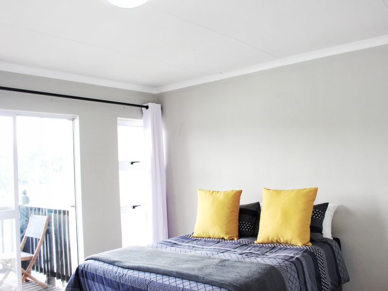 A bright bedroom featuring neutral walls, a ceiling light fixture, and a sliding glass door providing access to an outdoor balcony area.