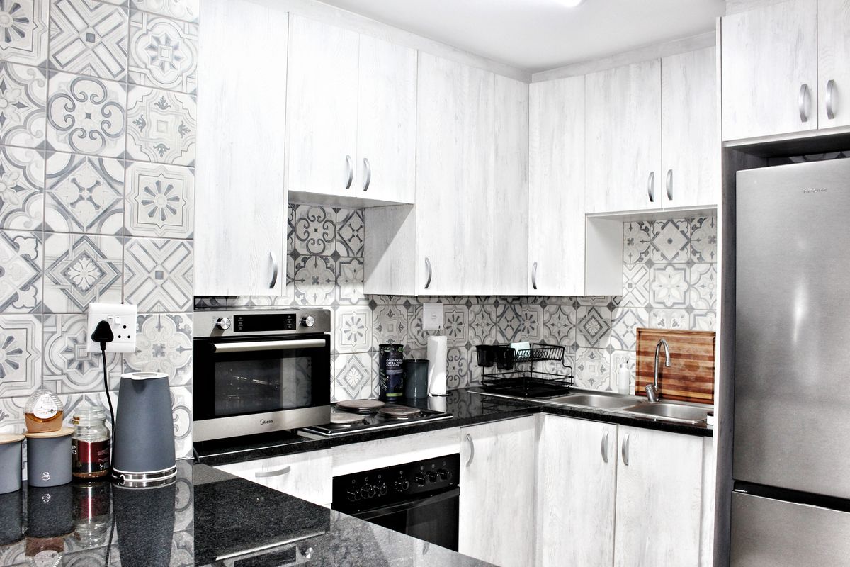 Modern kitchen featuring light wood-grain cabinetry, granite countertops, patterned tile backsplash, and built-in stainless steel oven and hob.