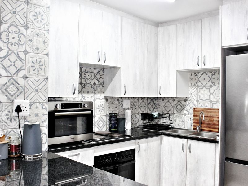 Modern kitchen featuring light wood-grain cabinetry, granite countertops, patterned tile backsplash, and built-in stainless steel oven and hob.