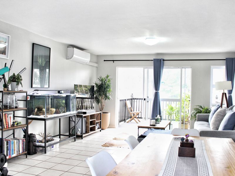 Bright open-plan living and dining area featuring tiled flooring, a wall-mounted air conditioner, and direct access to a private balcony through sliding glass doors.