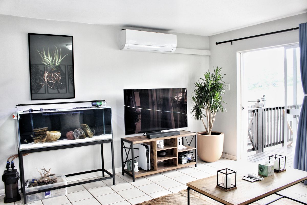 A bright living room featuring tiled flooring, a wall-mounted split-system air conditioner, and direct access to an outdoor balcony through a sliding glass door.