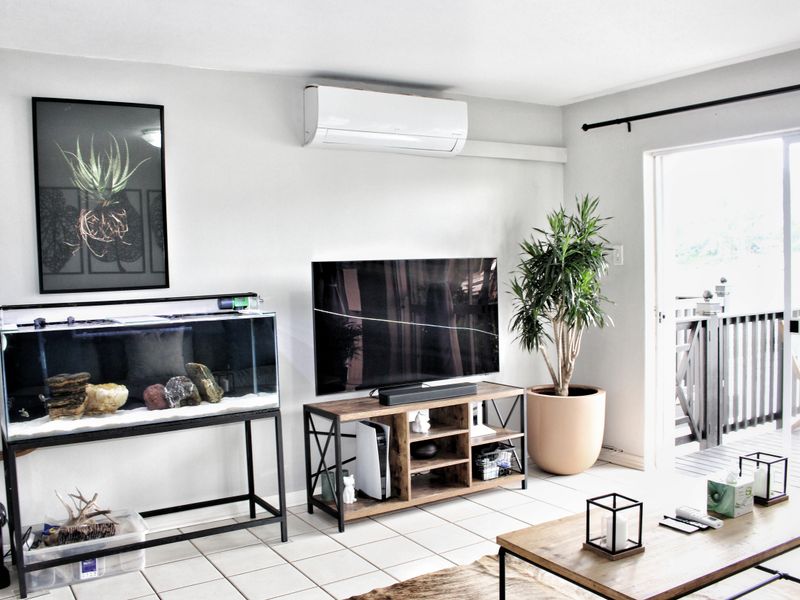 A bright living room featuring tiled flooring, a wall-mounted split-system air conditioner, and direct access to an outdoor balcony through a sliding glass door.