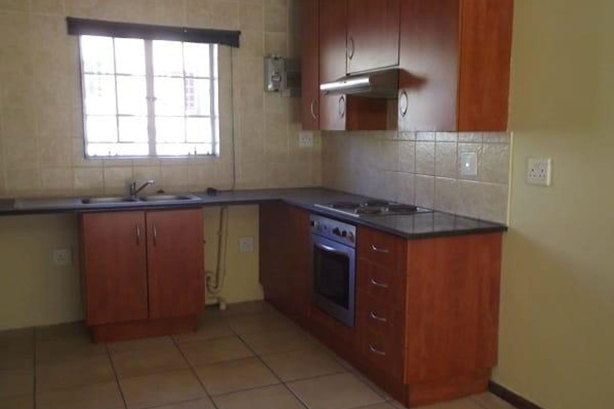 A functional kitchen featuring wooden cabinetry, tiled splashbacks, a built-in oven, hob, and extractor fan with a double sink.
