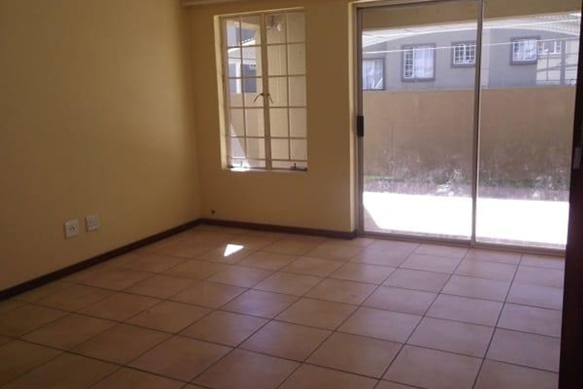 A bright, empty living area featuring tiled flooring, large windows, and a sliding glass door providing direct access to the outdoor space.