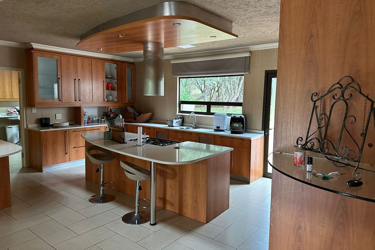 Spacious kitchen featuring wood-finish cabinetry, a central island with a gas cooktop, stainless steel extractor fan, and modern tiled flooring.