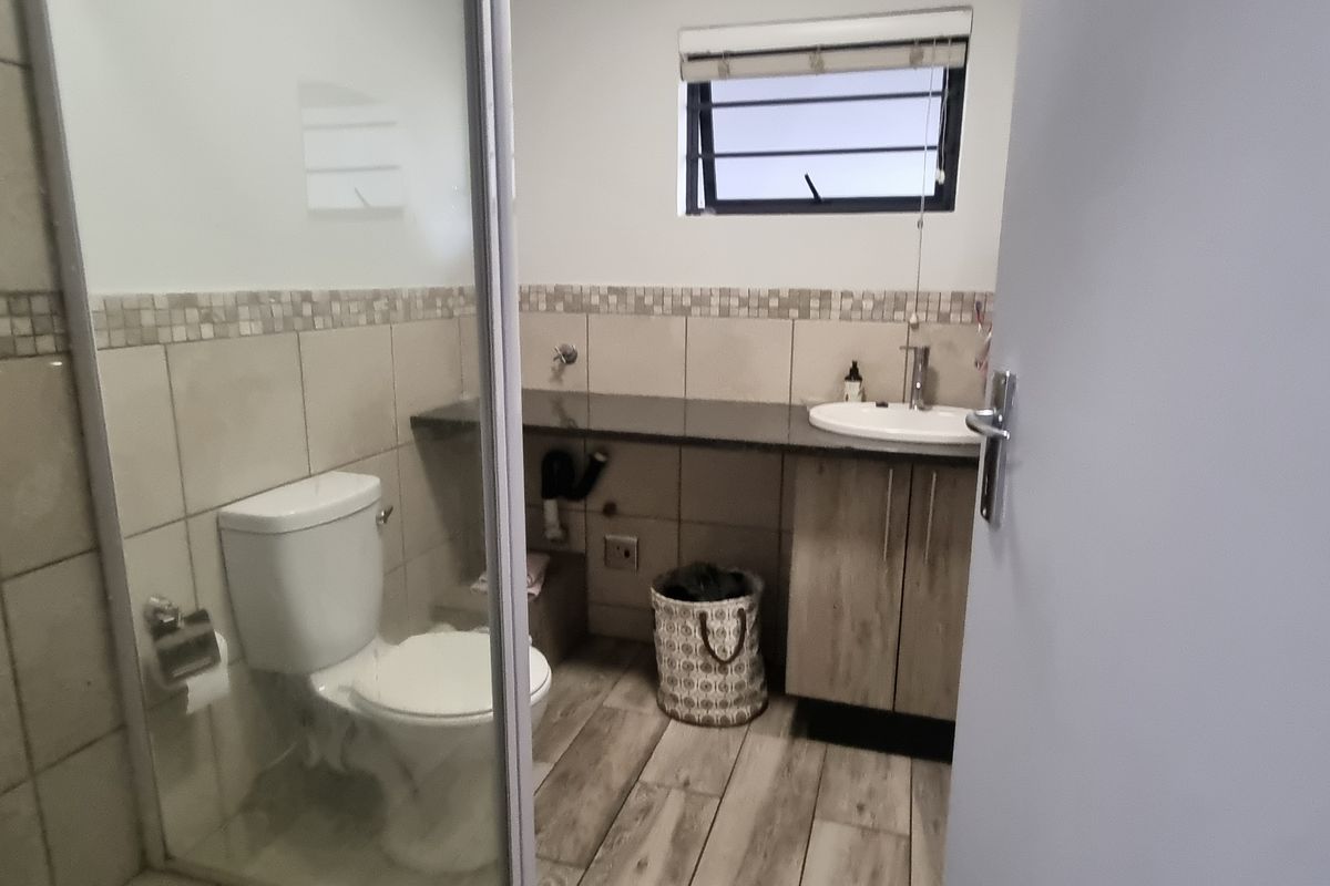 A functional bathroom featuring a shower enclosure, a vanity with a basin, tiled walls, and wood-look floor tiles.