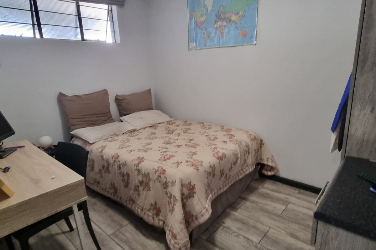 A compact bedroom featuring tiled flooring, a built-in wardrobe, and a window with security bars.