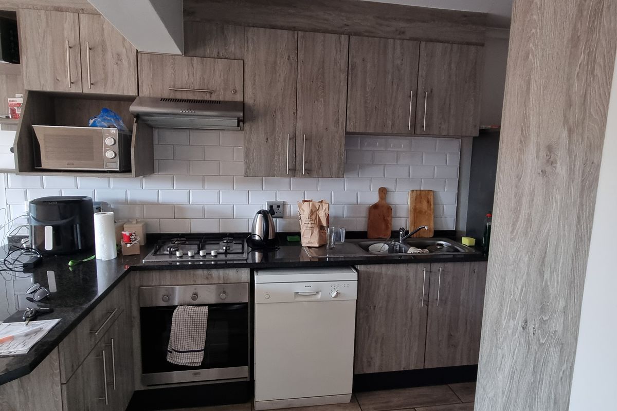 A functional kitchen featuring wood-look cabinetry, granite countertops, a subway tile backsplash, and built-in appliances including a gas hob and oven.