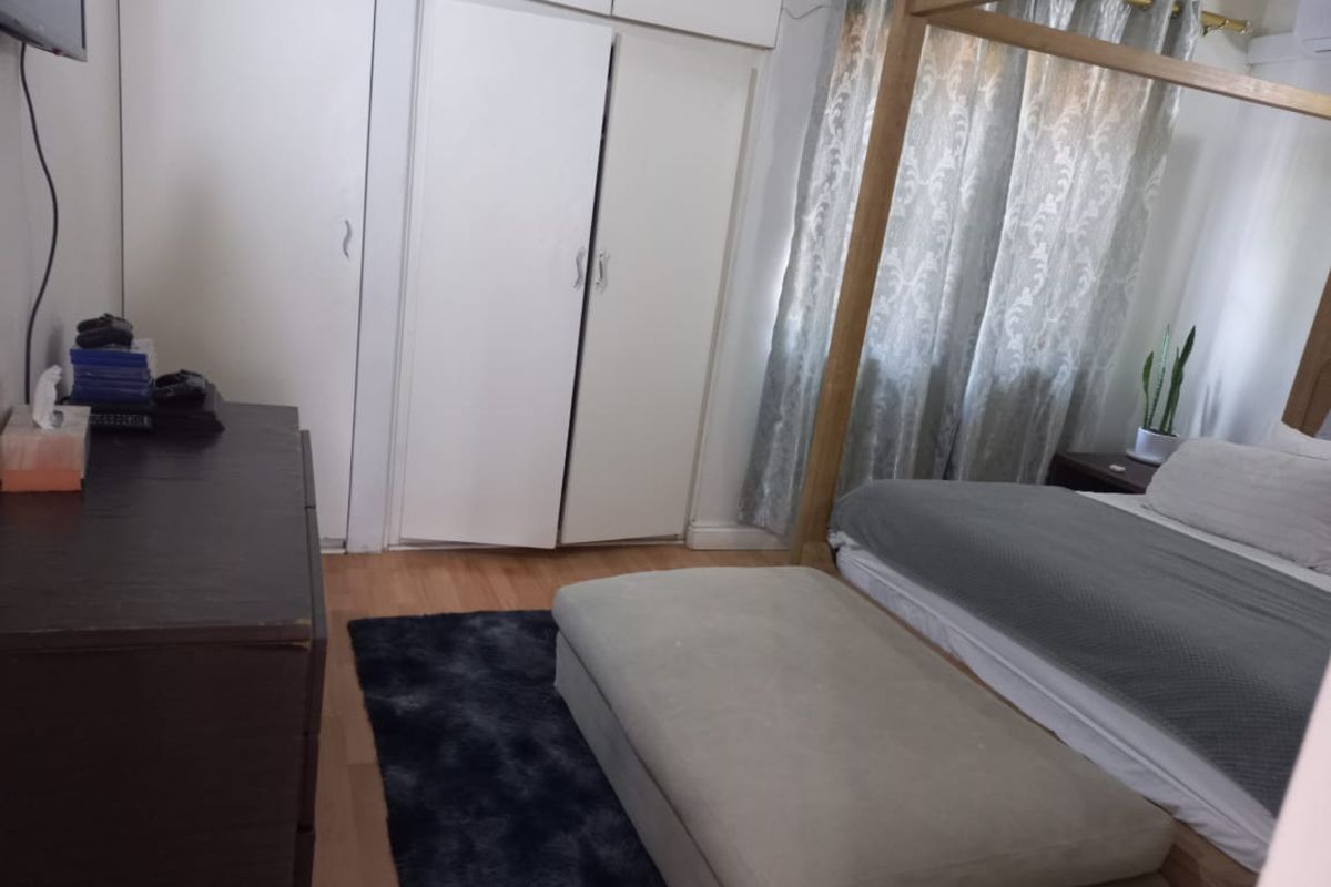 A bedroom featuring built-in white wardrobes with overhead storage and light-toned laminate flooring.