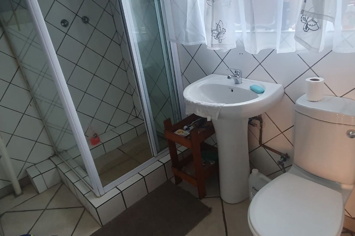 Compact bathroom featuring a shower enclosure, pedestal basin, and toilet with dated ceramic wall and floor tiling.
