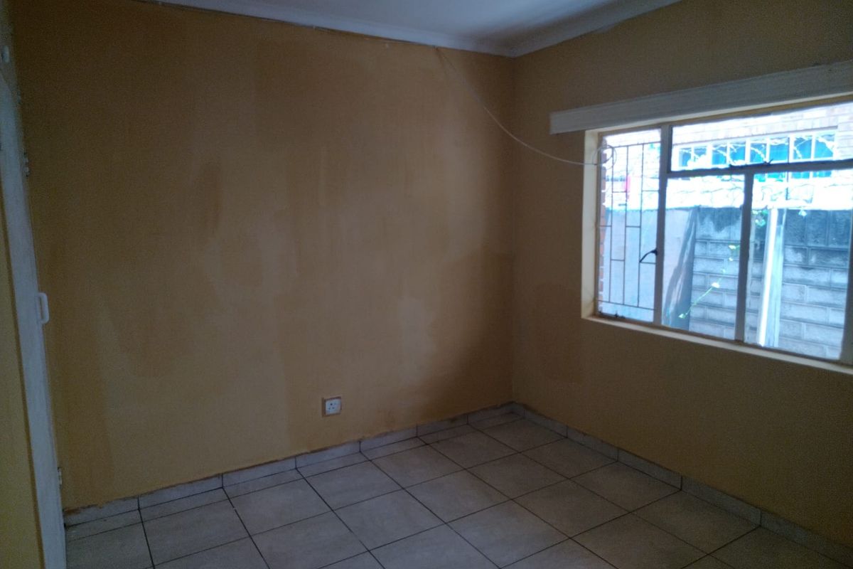 An empty bedroom featuring tiled flooring and security bars on the window, requiring cosmetic updates to the wall finishes.
