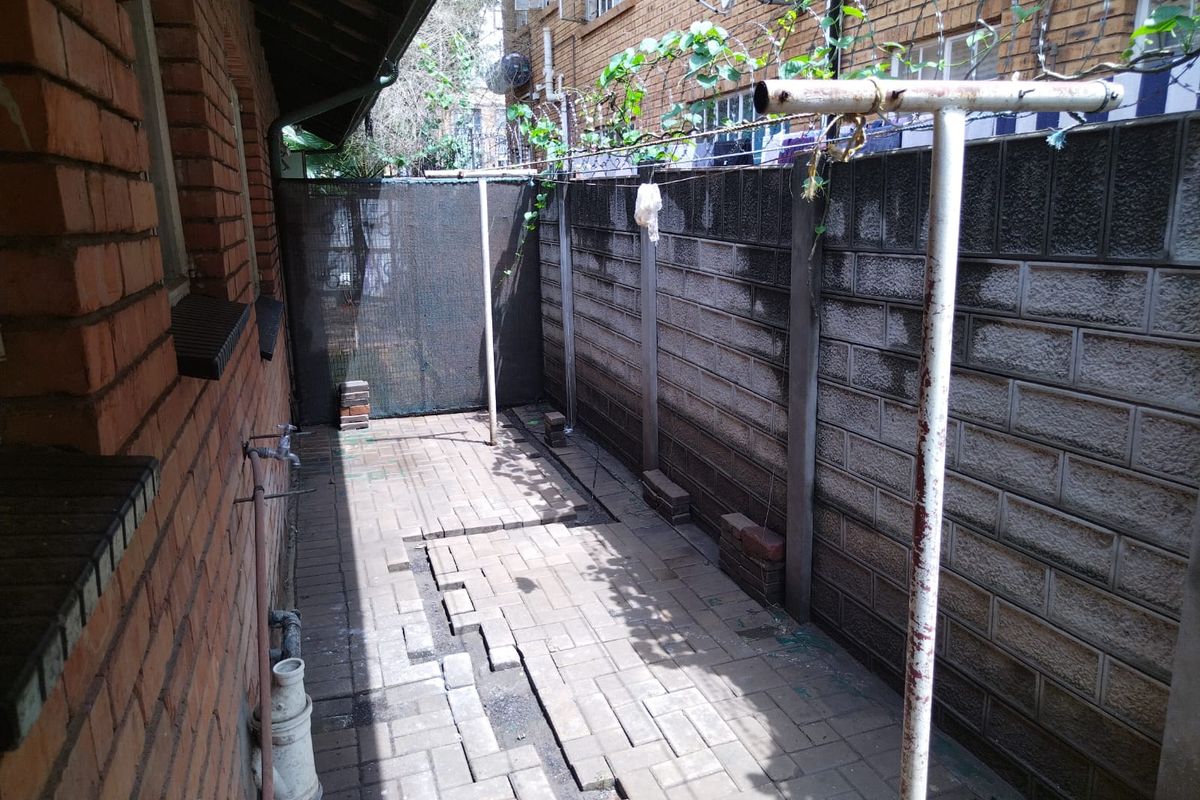A narrow rear exterior courtyard featuring brick paving, a boundary wall, and an external water tap, currently used as a utility area.