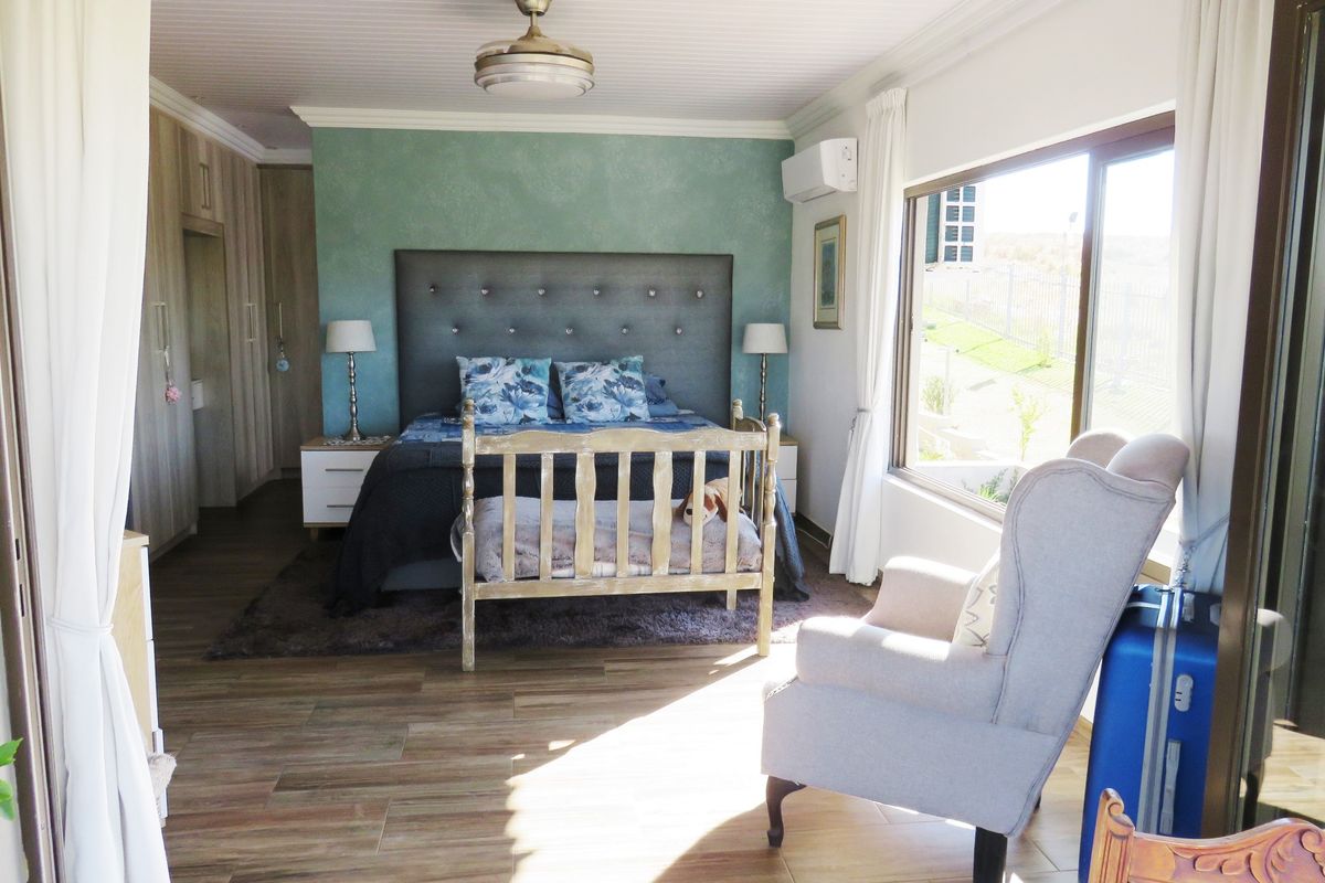 A well-lit bedroom featuring built-in cupboards, tiled flooring, a ceiling fan, and an air conditioning unit with views through a large sliding window.