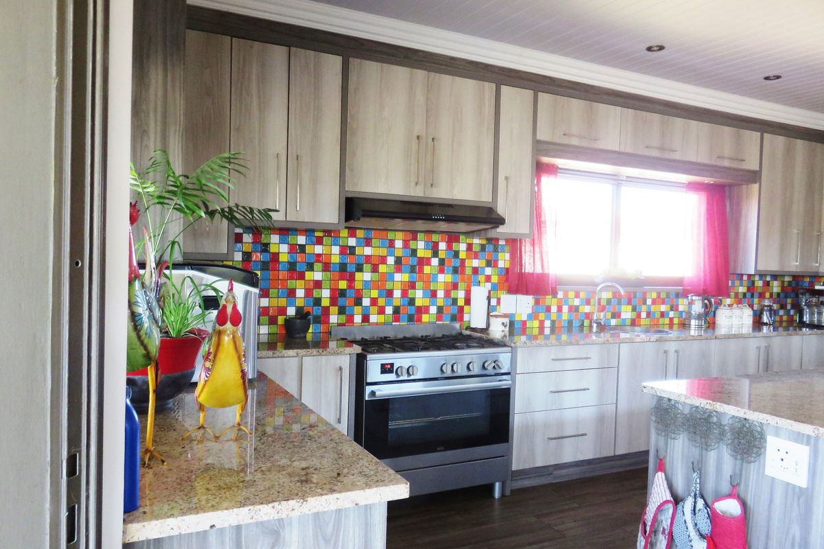 A functional kitchen featuring wood-look cabinetry, granite countertops, a gas stove with extractor fan, and a vibrant multi-colored mosaic tile backsplash.