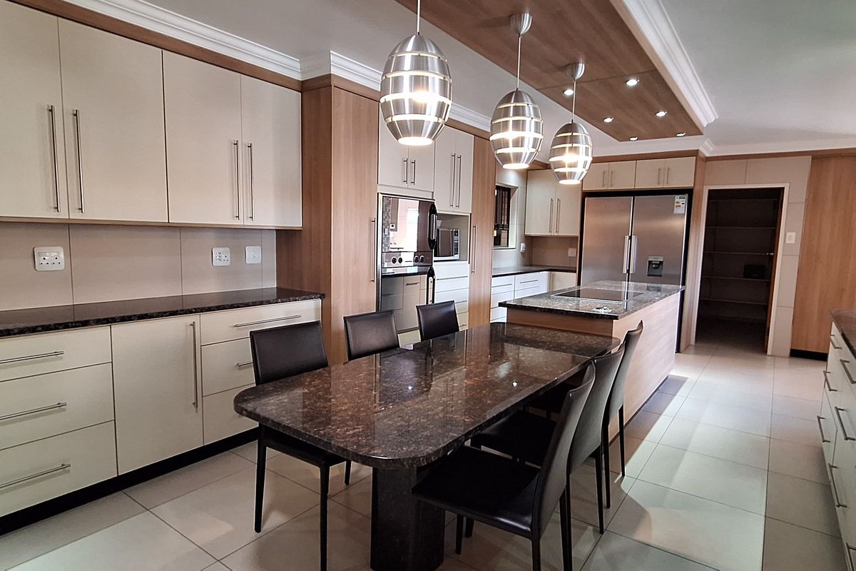Modern kitchen featuring extensive built-in cabinetry, granite countertops, a central island, and integrated appliances with a seamless transition to the scullery area.