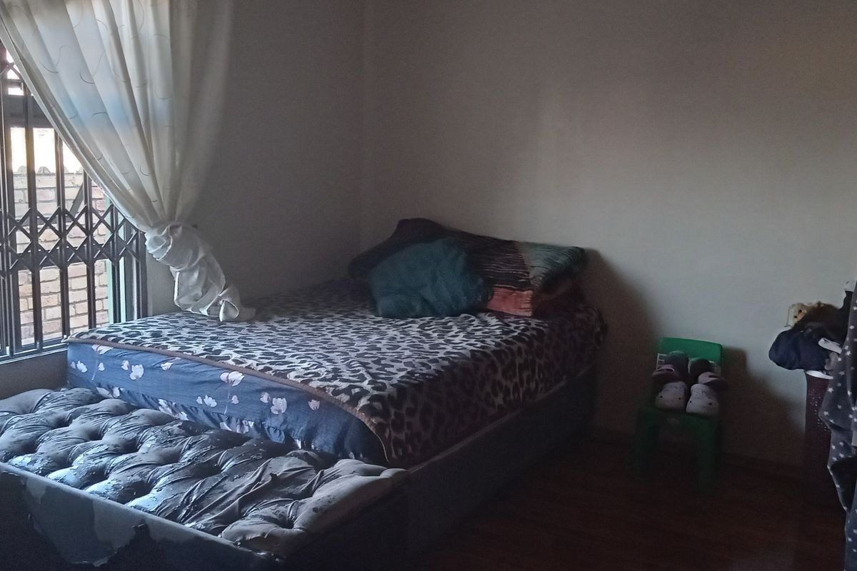 A standard bedroom featuring laminate flooring and a window fitted with a metal security gate.