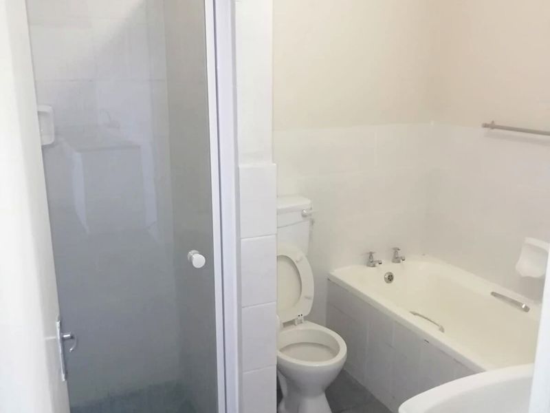A functional bathroom featuring a separate shower enclosure, bathtub, toilet, and washbasin with neutral wall tiles and grey floor tiles.