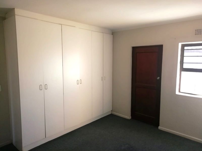 A clean, empty bedroom featuring built-in white cupboards, a dark timber door, and a louver window, providing a neutral space ready for personalization.