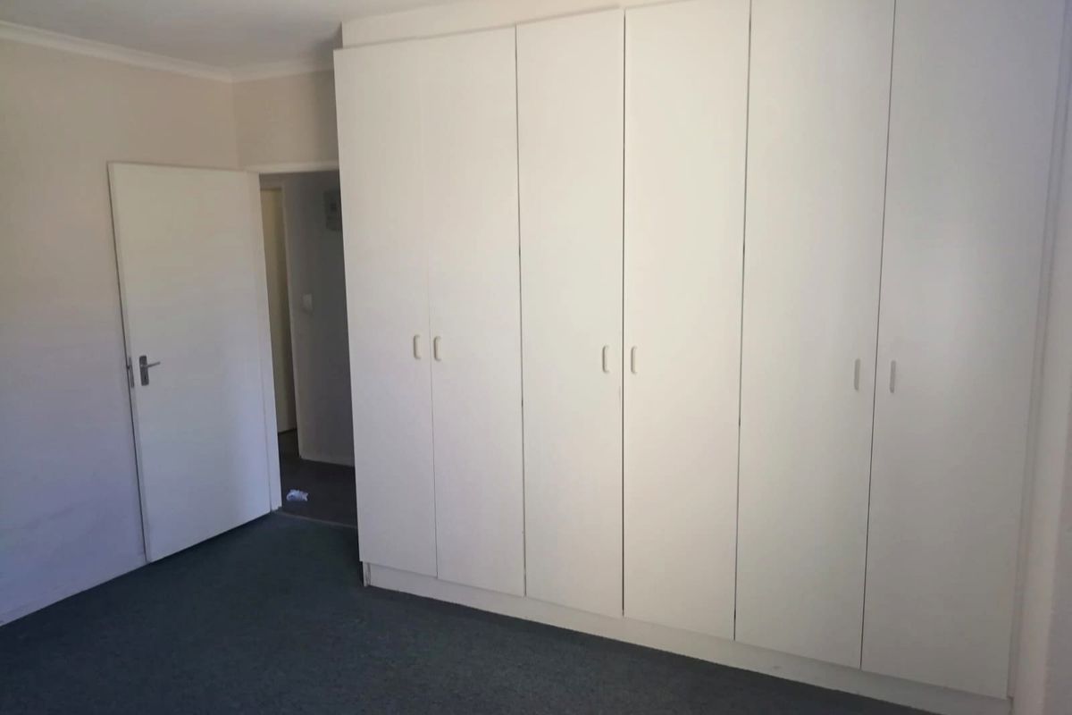 A clean, empty bedroom featuring neutral walls, carpeted flooring, and extensive built-in cupboard storage.