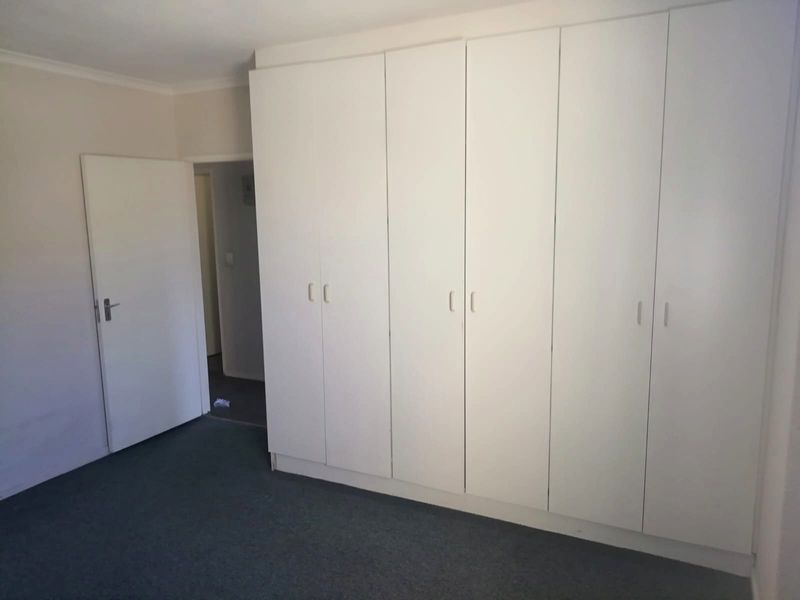 A clean, empty bedroom featuring neutral walls, carpeted flooring, and extensive built-in cupboard storage.