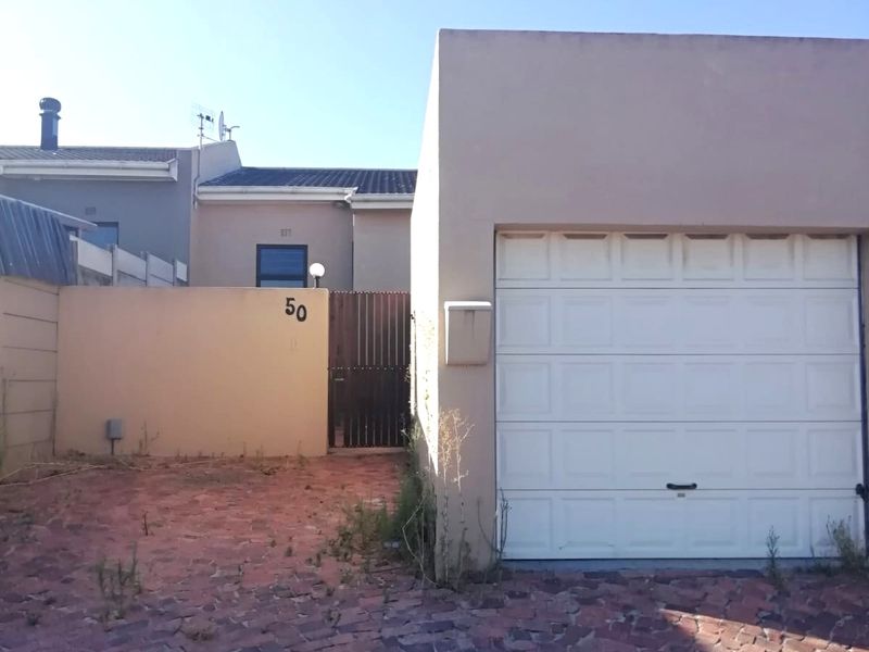 Front exterior view of the property featuring a single garage, paved driveway, and a gated pedestrian entrance with boundary wall.