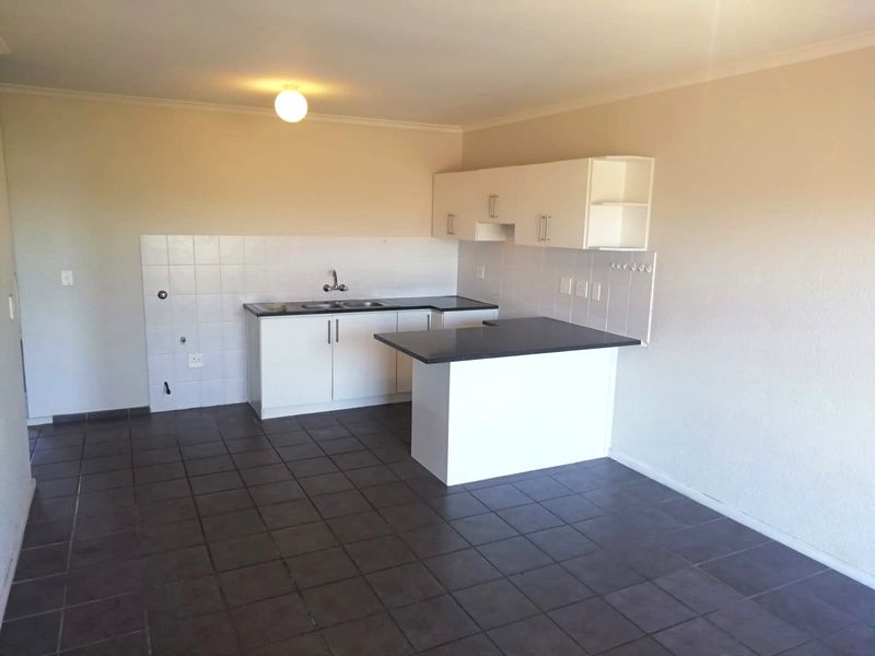 A clean, empty kitchen featuring white built-in cabinetry, dark countertops, tiled splashbacks, and dark floor tiles, offering a functional blank canvas.
