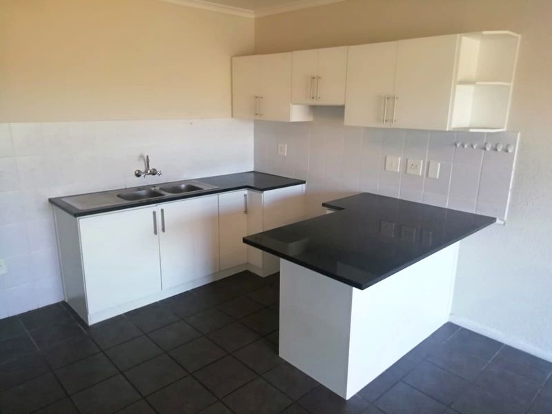 A clean, empty kitchen featuring white built-in cabinetry, dark countertops, a double bowl sink, and tiled flooring.