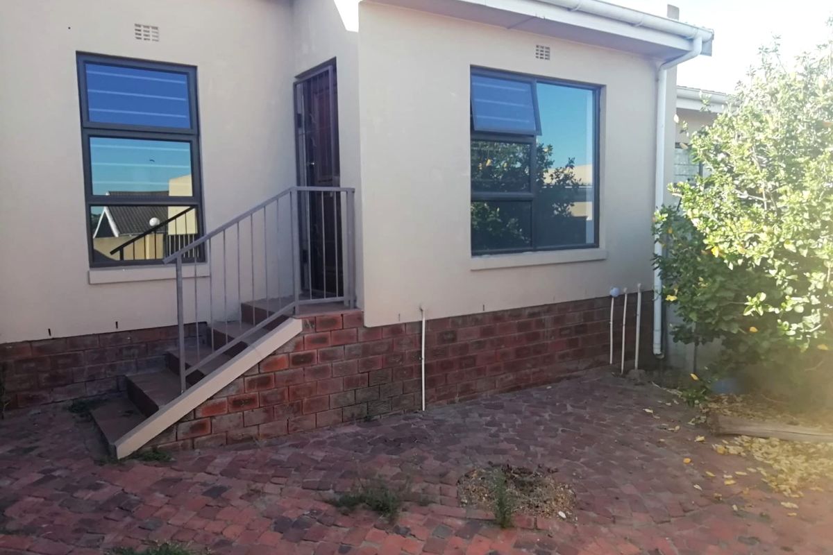 Rear exterior view of the property featuring brick paving, a small staircase with metal railing, and aluminium window frames.