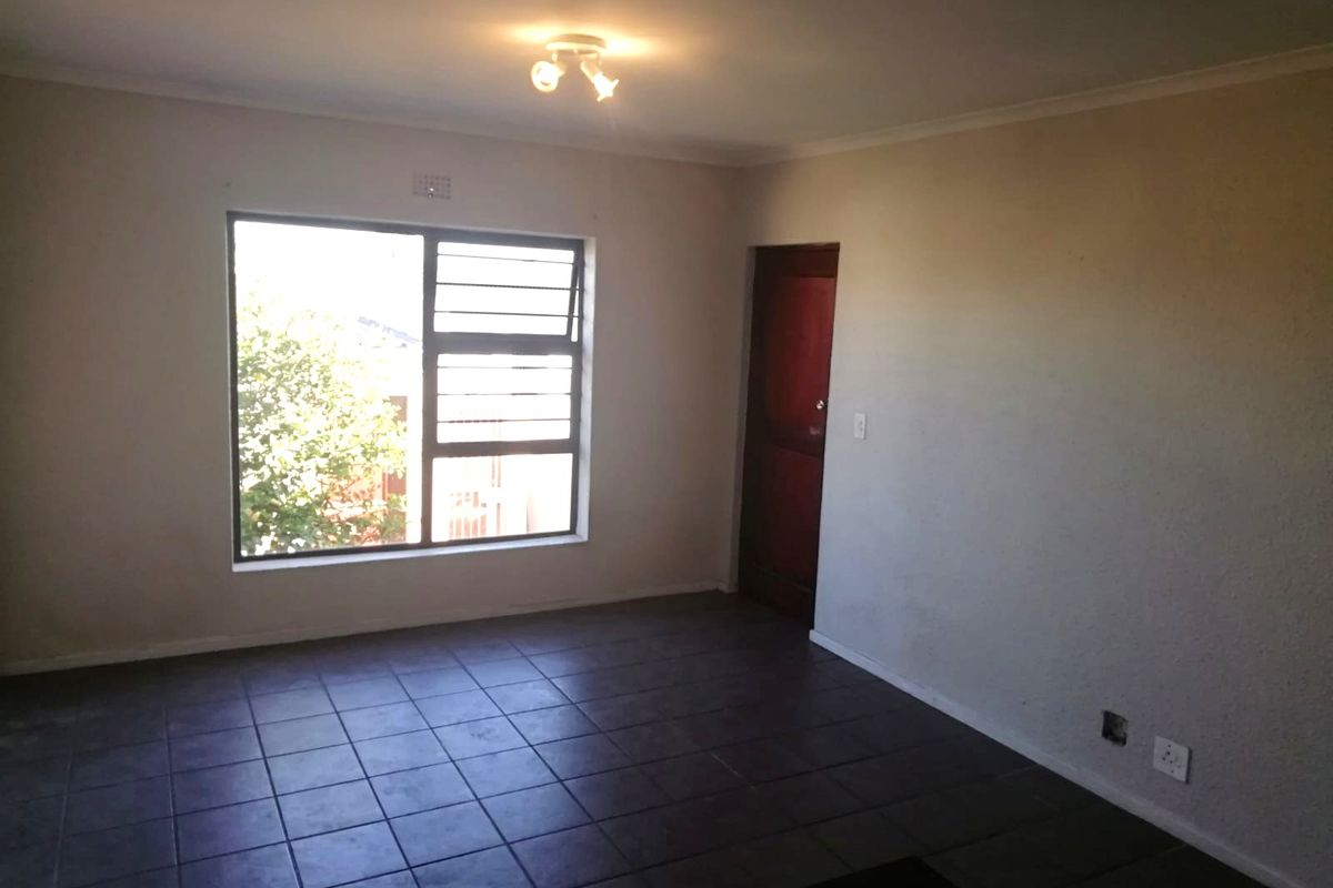 An empty living room featuring dark tiled flooring, a large window with security bars, and a simple ceiling light fixture.