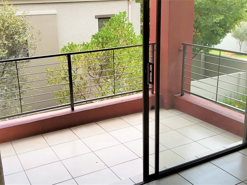 A private balcony featuring tiled flooring and a metal balustrade, accessible through a large sliding glass door.
