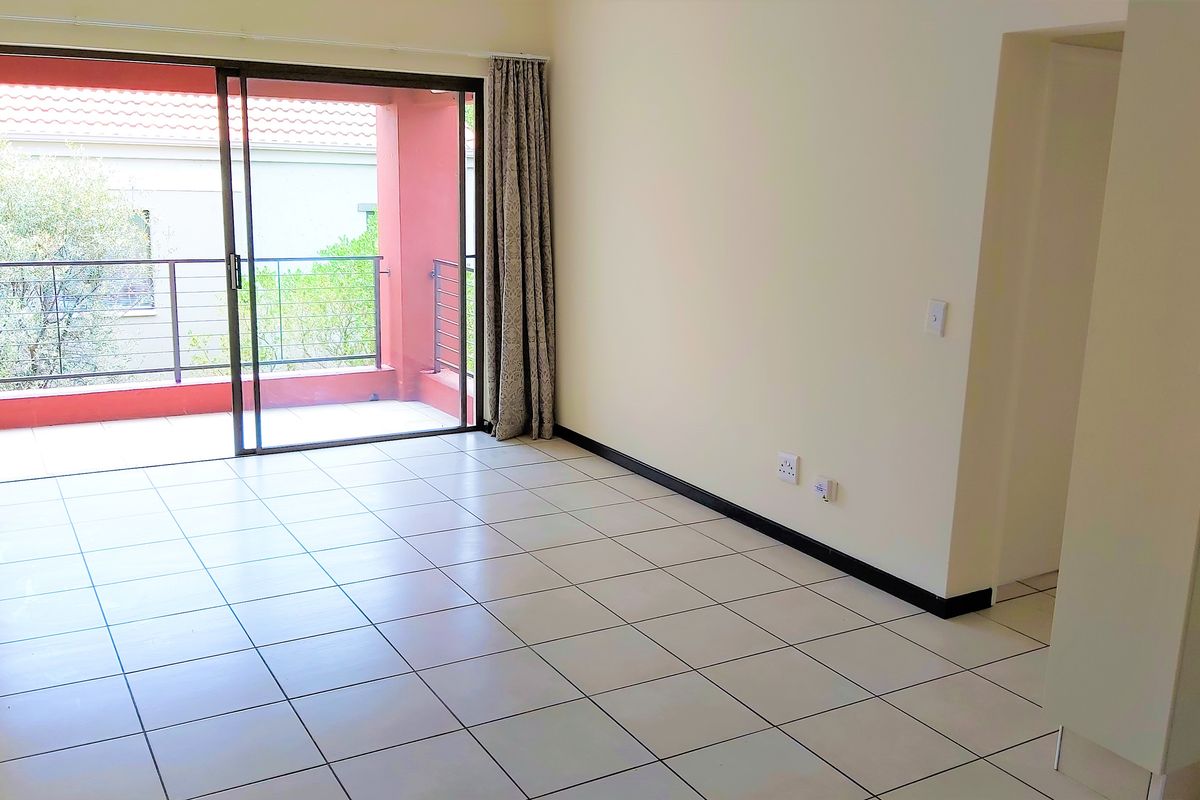 A bright, empty living room featuring neutral tiled flooring and a large sliding glass door providing direct access to a private balcony.