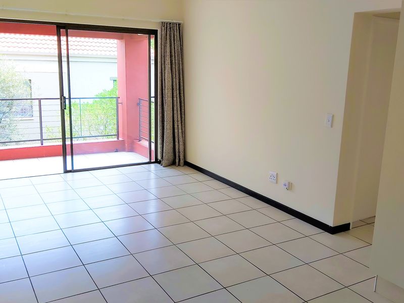 A bright, empty living room featuring neutral tiled flooring and a large sliding glass door providing direct access to a private balcony.