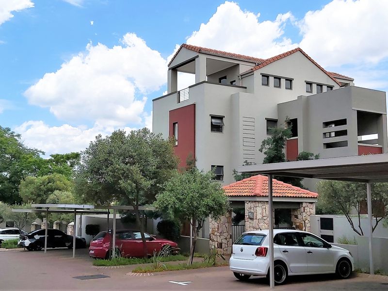 Exterior view of a multi-story apartment complex featuring modern architecture, stone accents, tiled roofing, and covered parking bays.