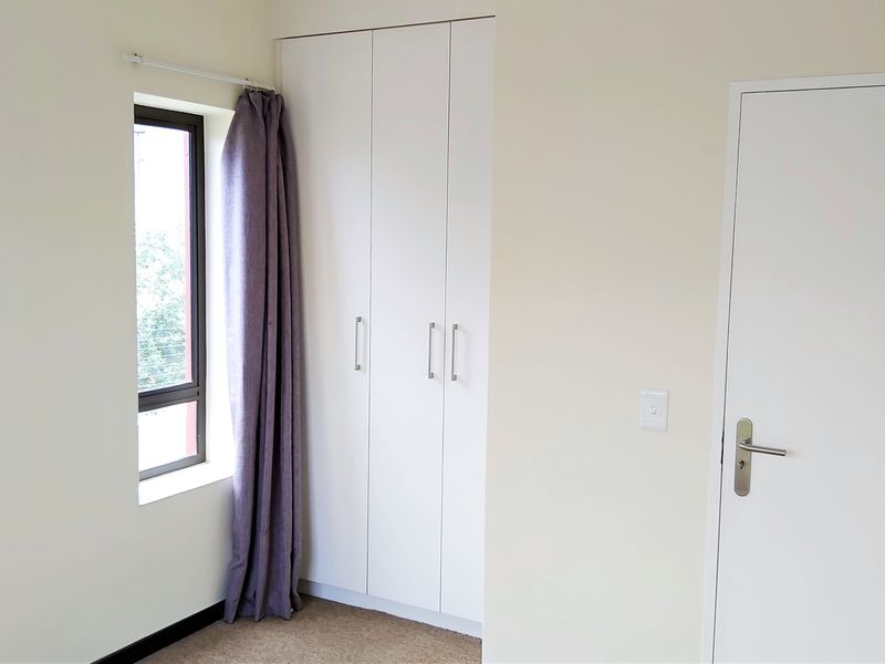 A clean, empty bedroom featuring neutral walls, carpet flooring, and a built-in wardrobe with white cabinetry.