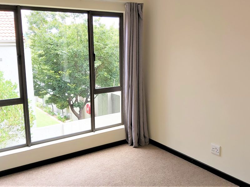 A bright, empty bedroom featuring large aluminium-framed windows, neutral carpeted flooring, and clean wall finishes, offering a blank canvas for personalization.