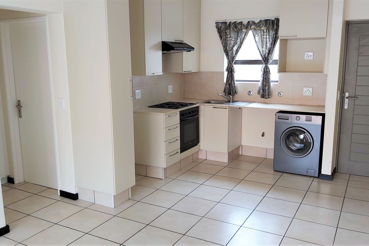 A functional kitchen featuring built-in cabinetry, an integrated oven and hob, extractor fan, and tiled flooring with space for a washing machine.