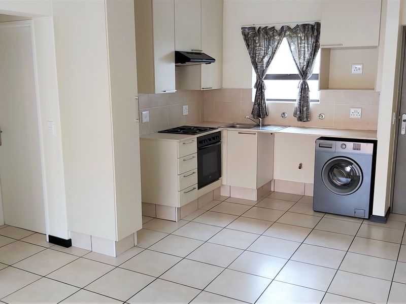 A functional kitchen featuring built-in cabinetry, an integrated oven and hob, extractor fan, and tiled flooring with space for a washing machine.