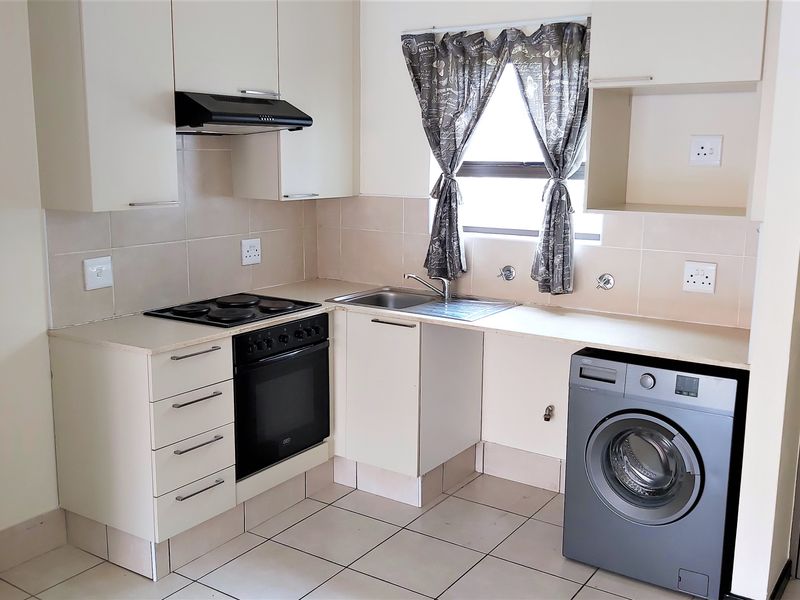 Compact kitchen featuring built-in cabinetry, electric stove with oven, extractor fan, tiled splashback, and dedicated plumbing for a washing machine.