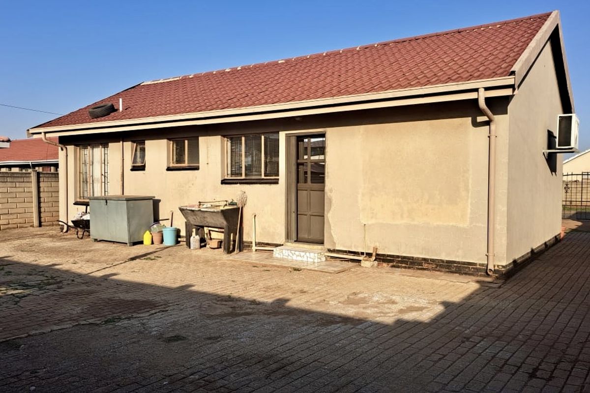 Rear view of the house featuring a tiled roof, paved yard area, and perimeter walling with security bars on the windows.