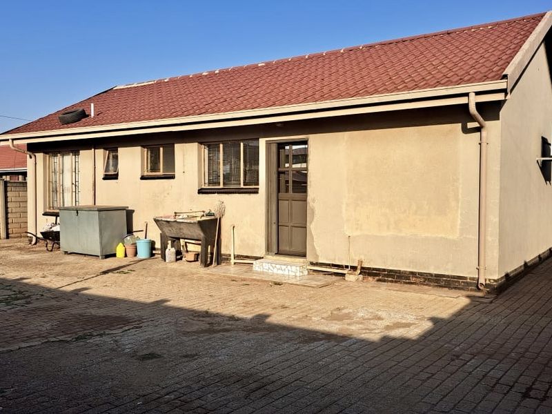 Rear view of the house featuring a tiled roof, paved yard area, and perimeter walling with security bars on the windows.
