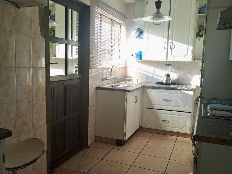 A functional kitchen featuring built-in cabinetry, tiled splashbacks, and a stainless steel sink, offering a practical layout with potential for modern cosmetic updates.