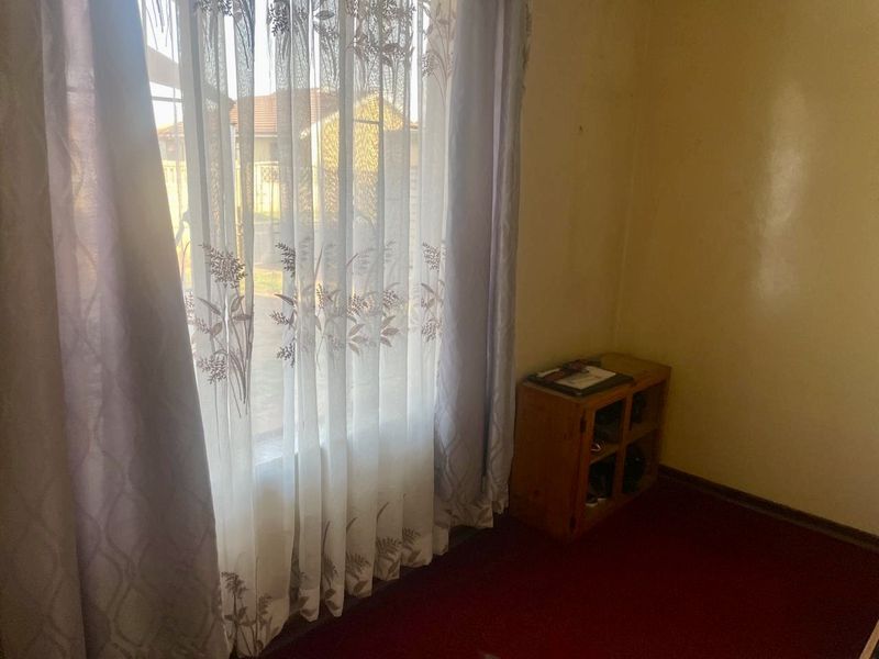 A simple bedroom space featuring a large window with curtains and carpeted flooring, offering a blank canvas for renovation.
