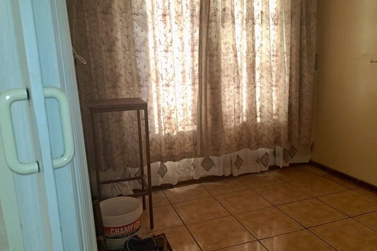 A vacant bedroom featuring tiled flooring and window curtain tracks, requiring cosmetic updates to the wall finishes.