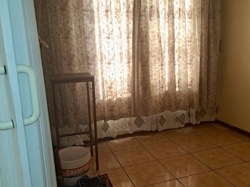 A vacant bedroom featuring tiled flooring and window curtain tracks, requiring cosmetic updates to the wall finishes.