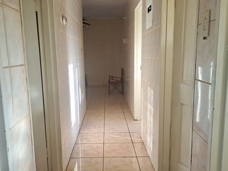 A tiled hallway connecting multiple rooms, featuring dated ceramic wall and floor tiles throughout.