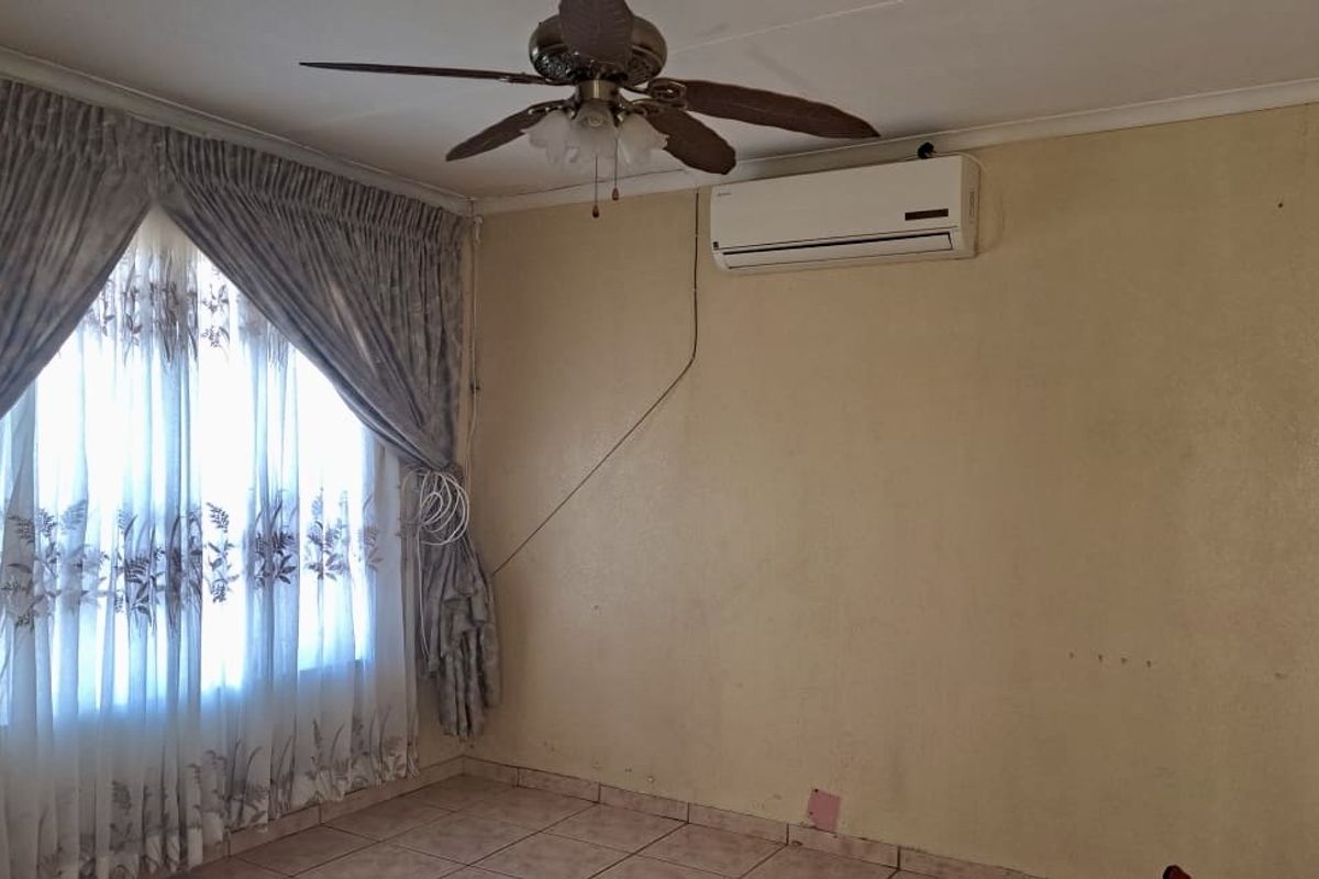 A living room featuring tiled flooring, a ceiling fan, and a wall-mounted air conditioning unit, requiring cosmetic updates to the wall finishes.