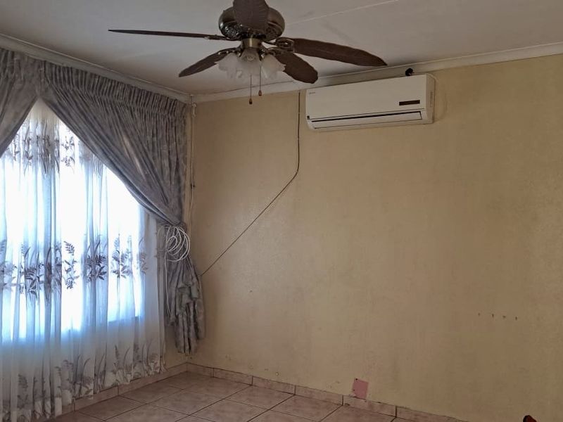A living room featuring tiled flooring, a ceiling fan, and a wall-mounted air conditioning unit, requiring cosmetic updates to the wall finishes.