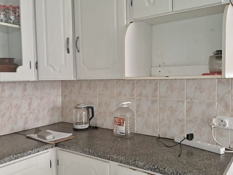 A dated kitchen area featuring laminate countertops, tiled backsplash, and traditional white cabinetry with glass-fronted display sections.