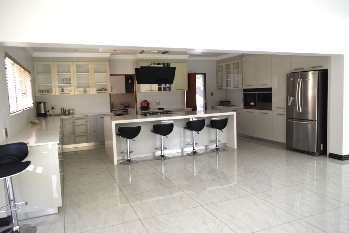Modern open-plan kitchen featuring a large central island, high-gloss cabinetry, integrated appliances, and polished porcelain floor tiles.